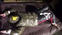 Watching Jill being tied on a bed wearing a shiny nylon rain jacket and a down jacket as well as a rain pants being double hooded and gagged with a ballgag (Video)