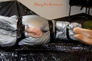 Mara tied and gagged with tape on bed wearing s shiny silver PVC sauna suit (Pics)