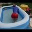 Mara playing with water in a small swimmingpool wearing a red shiny nylon shorts and a rain jacket (Video)