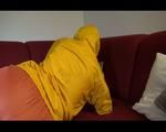 Lucy wearing an orange rain pants and a yellow rain jacket lolling on the sofa and reading a bit (Video)