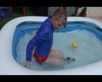 Mara playing with water in a small swimmingpool wearing a red shiny nylon shorts and a rain jacket (Video)