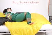 Jill tied and gagged with tape on bed wearing a shiny green nylon rainsuit (Pics)