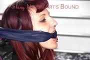 Mara tied and gagged on bed wearing a shiny purple down jacket and a blue rain pants (Pics)