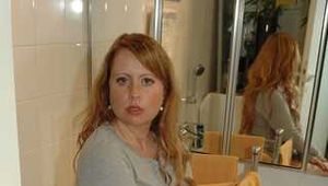 Chubby redhead Benita stripping out of a grey top and white stockings in the bathroom