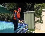 Mara wearing a sexy darkblue rain pants and rain jacket testing a life jacket in the swimmingpool (Video)