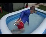 Mara playing with water in a small swimmingpool wearing a red shiny nylon shorts and a rain jacket (Video)