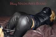 Sexy Sandra wearing a sexy shiny black rain pants and a sexy black down jacket with coat ties, gagges and hoodes herself on a bed with shiny nylon linen (Pics)