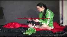 Lucy wearing a green shiny nylon shorts and a green rain jacket ties and gagges herself on a bed (Video)