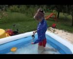 Mara playing with water in a small swimmingpool wearing a red shiny nylon shorts and a rain jacket (Video)