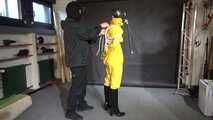See Lady M, bound in shiny yellow Rainsuit, wearing a latex Mask and a Gasmask