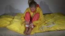 Watching Sandra  wearing an orange shiny nylon rain pants and a yellow shiny nylon rain jacket being tied and gagged on a bed with ropes and a clothgag (Video)