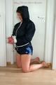 Katharina tied and gagged with a blue ball in a dark blue shiny nylon shorts with white stripes and a dark blue rain jacket