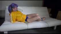 Mara with blue hairs wearing a sexy blue/yellow shiny nylon shorts and a yellow rain jacket tied and gagged with ropes and a ball gag on the sofa (Video)
