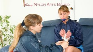 Leoni ties and gagges an archive girl on the sofa both wearing shiny nylon shorts and rainwear (Pics)