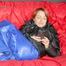 Sonja wearing a blue shiny nylon raver pants and a black down jacket posing and lollingn on the sofa (Pics)