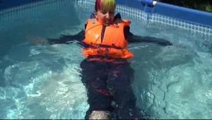 Mara wearing a sexy darkblue rain pants and rain jacket testing a life jacket in the swimmingpool (Video)