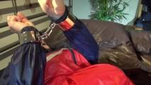 Jill tied and gagged on bed with chains and cuffs wearing shiny nylon shorts and a rain jacket (Video)