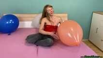 sitpopping nine U16 balloons on the bed