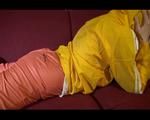 Lucy wearing an orange rain pants and a yellow rain jacket lolling on the sofa and reading a bit (Video)