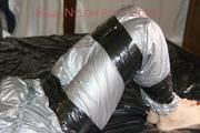 Pia tied and gagged with tape on a bed wearing a sexy silver rainwear combination (Pics) 