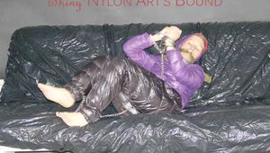 Sandra tied and gagged on a sofa with cuffs and a pillory wearing hot purple down jacket and black down pants (Pics)