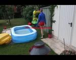 Mara playing with water in a small swimmingpool wearing a red shiny nylon shorts and a rain jacket (Video)