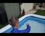 Mara playing with water in a small swimmingpool wearing a red shiny nylon shorts and a rain jacket (Video)