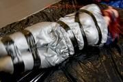 Mara tied and gagged with tape on bed wearing s shiny silver PVC sauna suit (Pics)