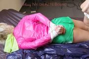 Pia in a green shiny nylon shorts with white stripes and a pink rain jacket tied and gagged in a bed (Pics)