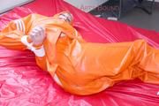 Pia tied and gagged in bed in a orange rainsuit and a red gag (Pics)