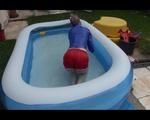 Mara playing with water in a small swimmingpool wearing a red shiny nylon shorts and a rain jacket (Video)