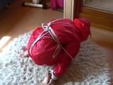 Black haired archive girl tied, gagged and hooded on the floor wearing a shiny red nylon shorts and a shiny red rain jacket (Video)