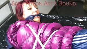Mara tied and gagged on bed wearing a shiny purple down jacket and a blue rain pants (Pics)