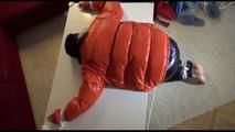 Mara tied and gagged on a table wearing a sexy black down pants and an orange down jacket (Video)