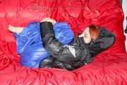 Sonja wearing a blue shiny nylon raver pants and a black down jacket posing and lollingn on the sofa (Pics)