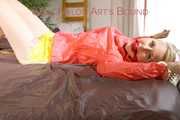 Mara tied and gagged with chains and cuffs on a bed wearing a superhot yellow shiny nylon shorts and an orange rain jacket (Pics)