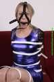 Sophie bound with Leatherbelts and Harnessgagged wearing a shiny purple Dress