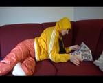 Lucy wearing an orange rain pants and a yellow rain jacket lolling on the sofa and reading a bit (Video)