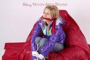 Samantha in grey rainsuit and purple down jacket tied and gagged on a red chair (pics)