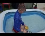 Mara playing with water in a small swimmingpool wearing a red shiny nylon shorts and a rain jacket (Video)