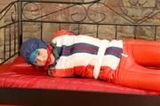 Mara tied, gagged and hooded on bed wearing a shiny red/blue/white striped old school down jacket and a skibib in red (Pics)