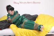 Jill tied and gagged with tape on bed wearing a shiny green nylon rainsuit (Pics)