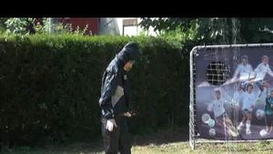 Mara wearing sexy black shiny rainwear while playing with the water of the sprinkler (Video)