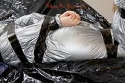 Mara tied and gagged with tape on bed wearing s shiny silver PVC sauna suit (Pics)