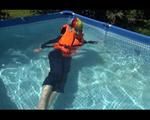 Mara wearing a sexy darkblue rain pants and rain jacket testing a life jacket in the swimmingpool (Video)