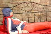 Mara tied, gagged and hooded on bed wearing a shiny red/blue/white striped old school down jacket and a skibib in red (Pics)